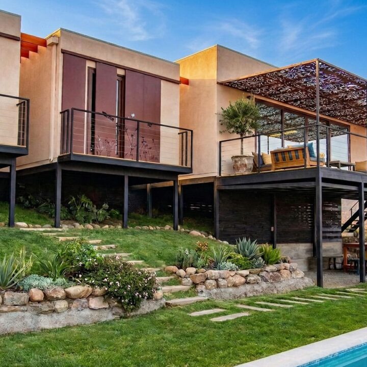 Fachada de Casa Tipo CH de Constructora Riegen en Hacienda Chacabuco Colina con terrazas, jardín de agaves, piscina y cordillera bajo cielo azul
